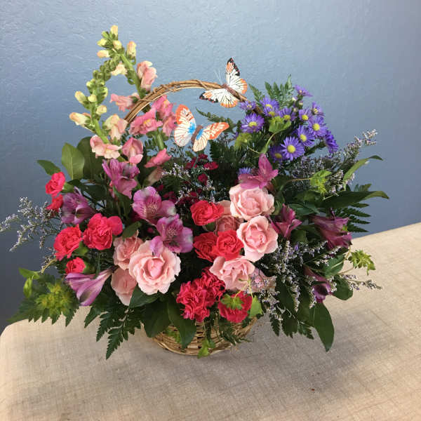Basket arrangement of pink and purple flowers with butterfly picks