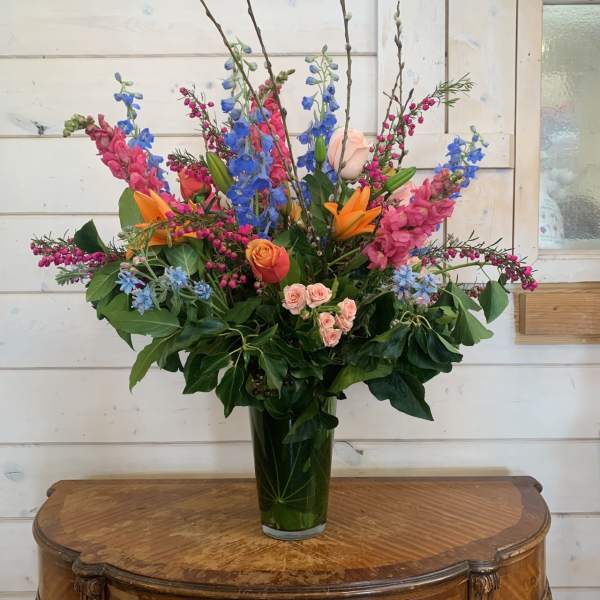 Tall mixed bouquet in a glass vase with blue, pink, orange, and peach flowers