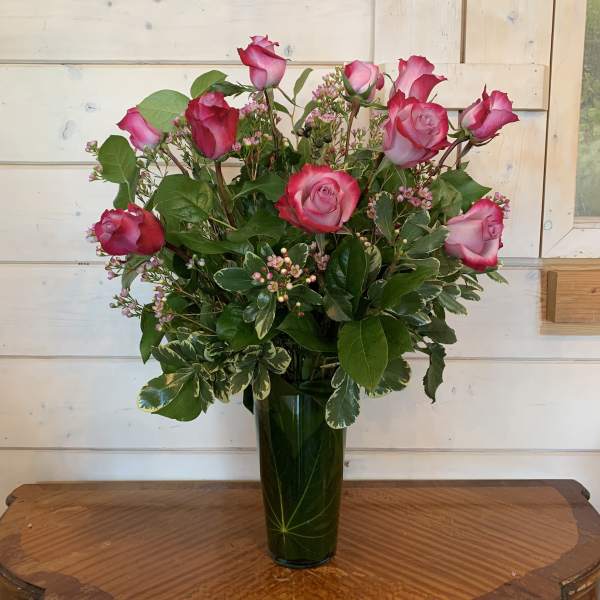 Pink roses arranged in a tall glass vase with mixed greenery