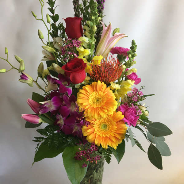 Tall mixed bouquet in a clear glass vase with red roses and bright blooms