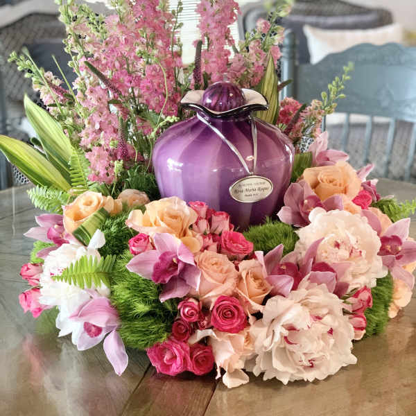 Pink and peach floral arrangement around a purple urn on a table