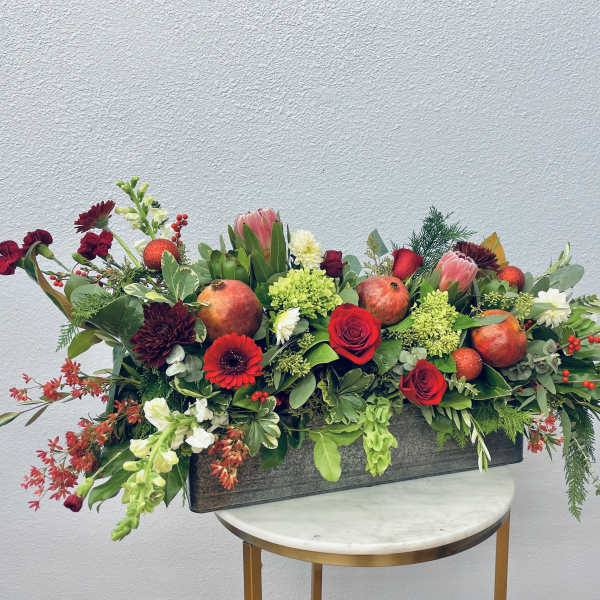 Long rectangular floral arrangement with red and pink blooms and pomegranates