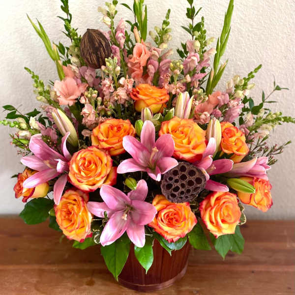 Orange roses and pink lilies in a wooden vase arrangement
