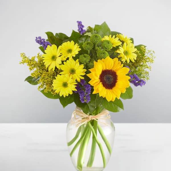 Yellow daisies and a sunflower in a glass vase