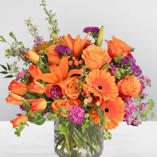 Orange flowers in a clear glass vase with purple accents
