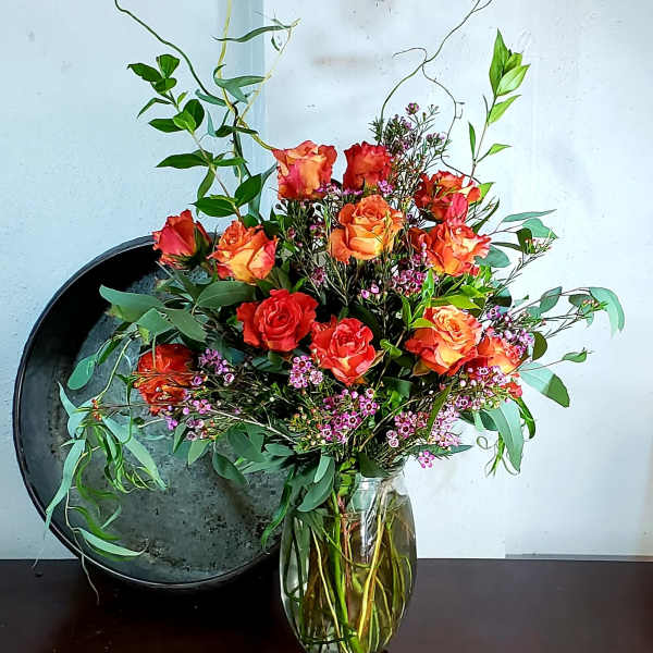 Orange and red roses in a clear glass vase with airy greenery