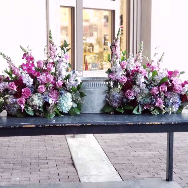 Two pink and lavender floral sprays flank a metal urn on a table