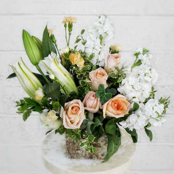 Peach roses and white lilies in a rustic container