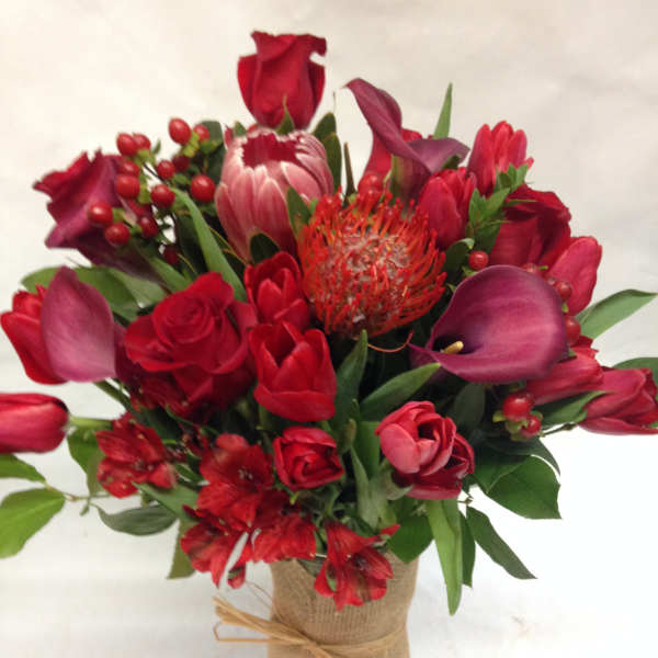 Red floral bouquet with roses, tulips, and calla lilies in a burlap-wrapped vase