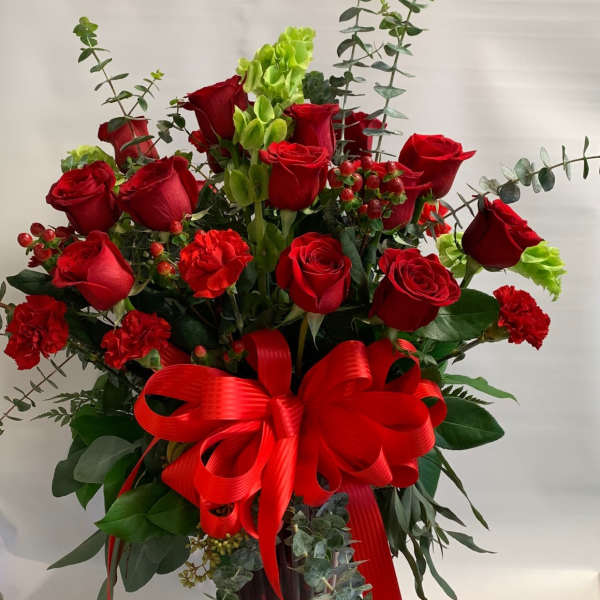 Red roses and carnations in a red glass vase with a large red bow