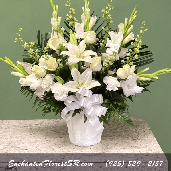 White lilies and carnations in a white vase with a ribbon bow