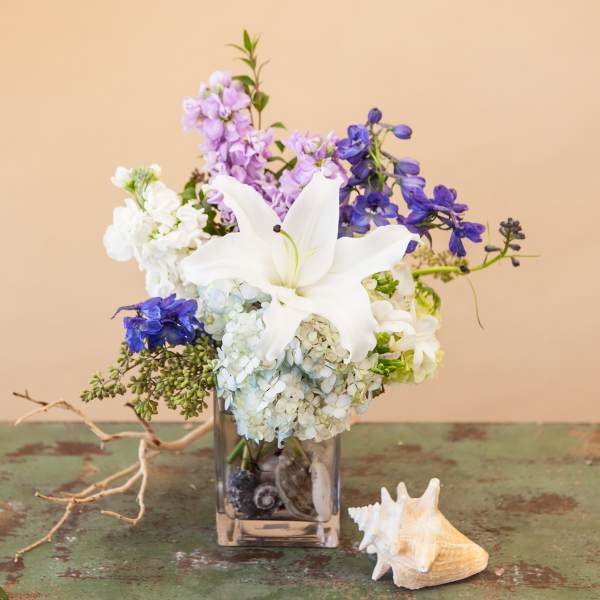 White lily bouquet with blue and lavender flowers in a glass vase