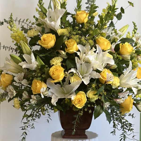 Large arrangement of yellow roses, yellow carnations, and white lilies in a brown urn vase