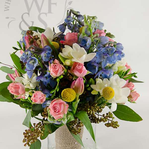 Mixed bouquet of pink, white, and blue flowers in a glass vase