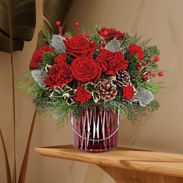 Red roses and carnations in a glass vase with pinecones and berries