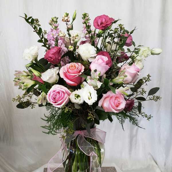 Pink and white rose bouquet in a glass vase with a pink ribbon