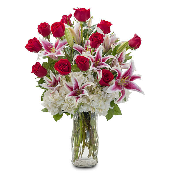 Tall arrangement of red roses, pink lilies, and white hydrangeas in a clear glass vase