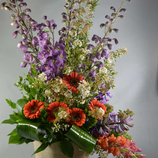 Tall mixed flower arrangement in a woven basket with orange and purple blooms