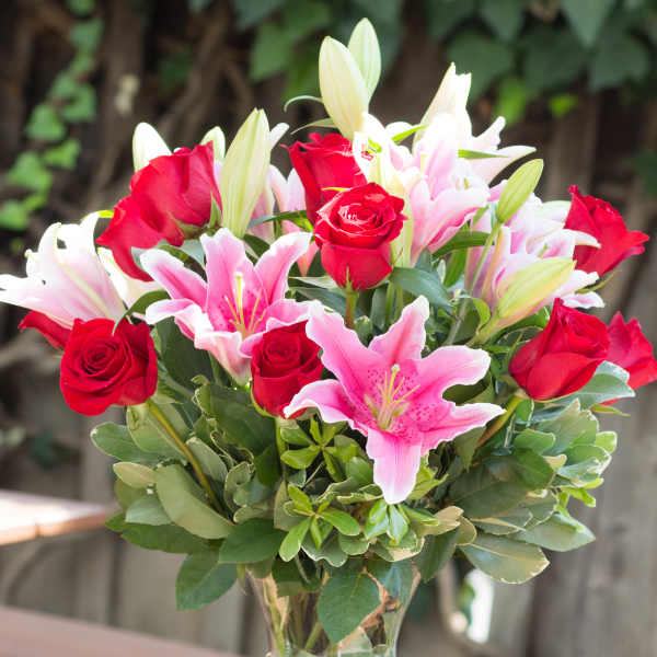 Bouquet of red roses and pink lilies in a clear glass vase