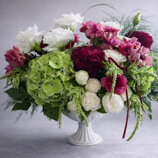 Mixed bouquet in a white pedestal vase with green hydrangea, white roses, and pink blooms