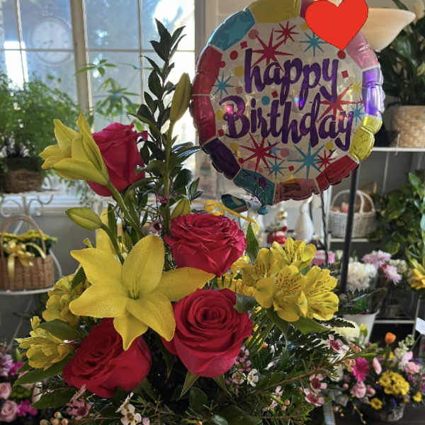 Birthday bouquet of red roses and yellow lilies in a glass vase with a balloon