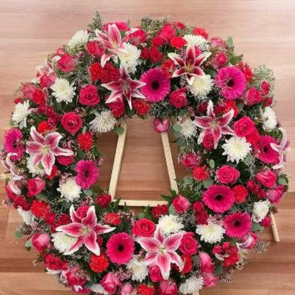 Heart-shaped floral wreath on a wooden easel with pink, red, and white blooms