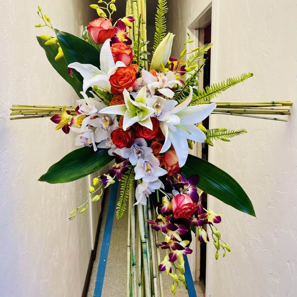 Tall floral standing spray with red roses, white lilies, and orchids on bamboo