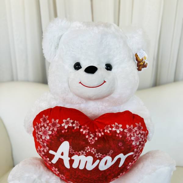 White teddy bear holding a red heart pillow with the word Amor