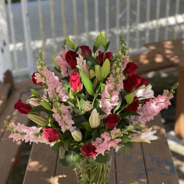 Bouquet of red roses, pink snapdragons, and white lilies in a glass vase