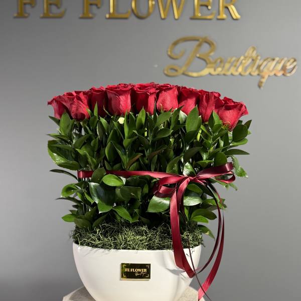 Red roses arranged in a white vase with a burgundy ribbon