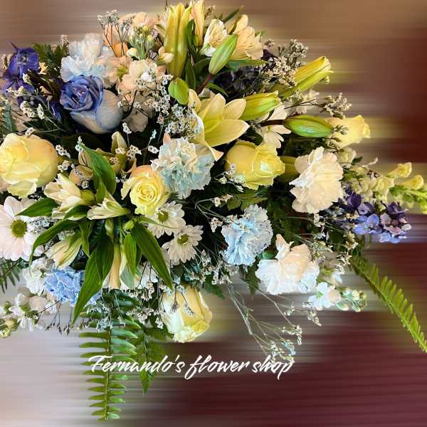 Rounded arrangement of yellow roses, white lilies, daisies and blue flowers in soft pastel tones