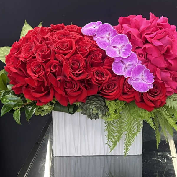 Red roses and pink hydrangeas with purple orchids in a white vase