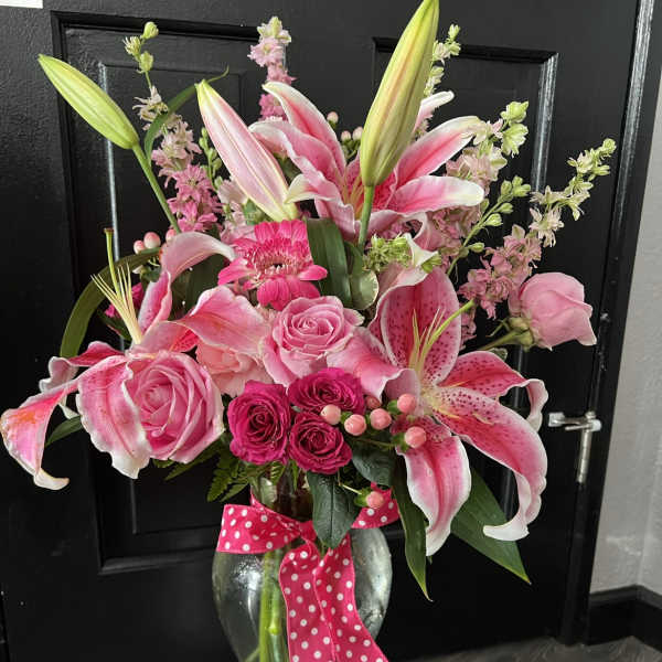 Pink lilies and roses arranged in a glass vase with a polka-dot ribbon
