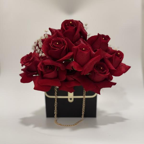 Red rose arrangement in a black gift box with a gold chain handle