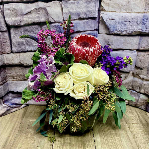 Bouquet with cream roses, a red protea, and purple flowers