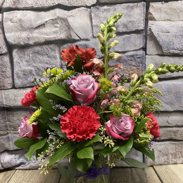 Mixed bouquet of roses, carnations, and snapdragons in a glass vase