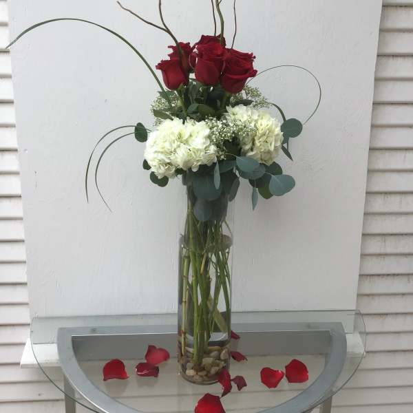 Tall vase arrangement of red roses and white hydrangeas with curly branches