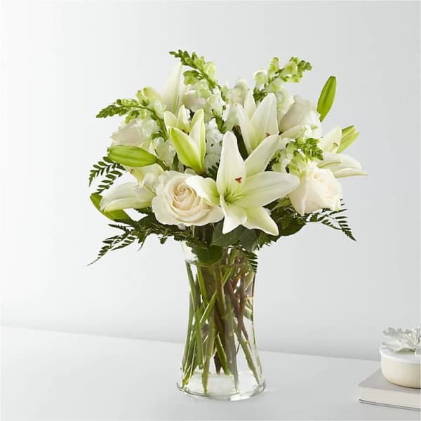 Arrangement of white lilies, roses, and snapdragons in a clear glass vase