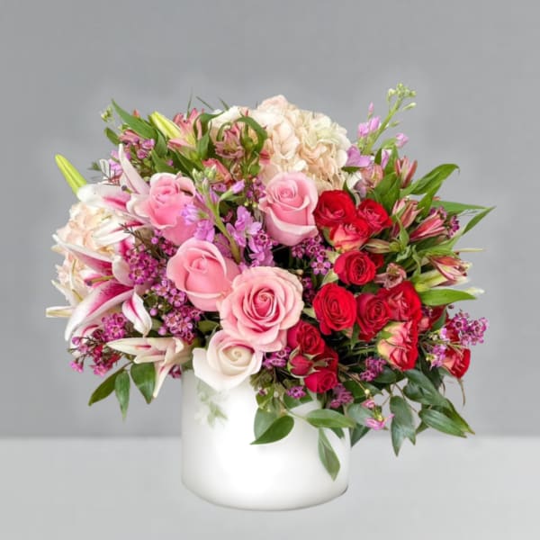 Mixed pink and red flower arrangement in a white vase