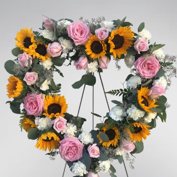 Heart-shaped floral wreath with pink roses, sunflowers, and white carnations