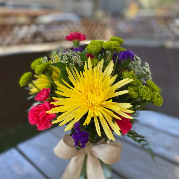 Bouquet of yellow, pink, green, and purple flowers tied with a beige ribbon