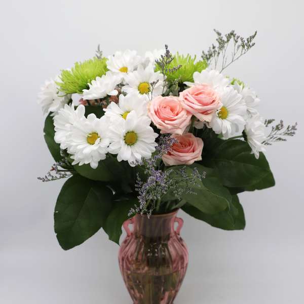 Pink roses and white daisies arranged in a pink glass vase