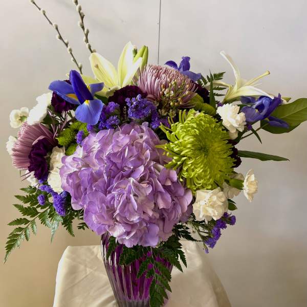 Bouquet of purple, white, and green flowers in a purple glass vase