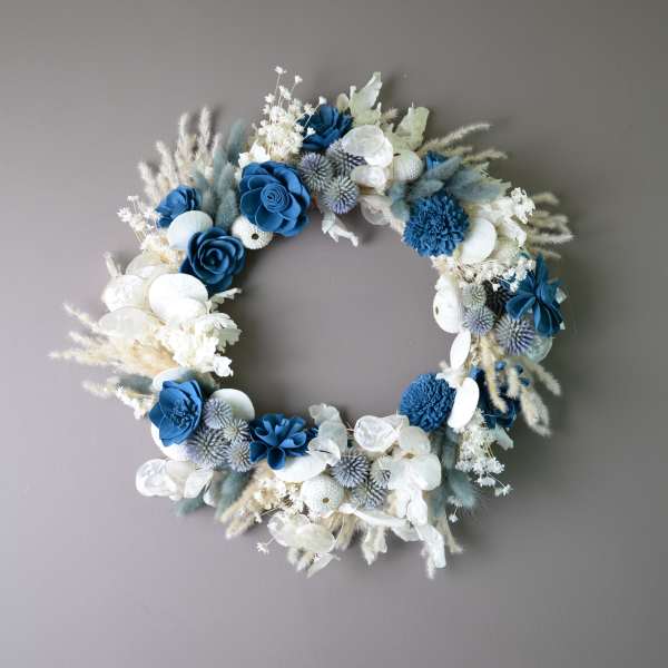 Blue and white floral wreath with dried accents on a gray wall