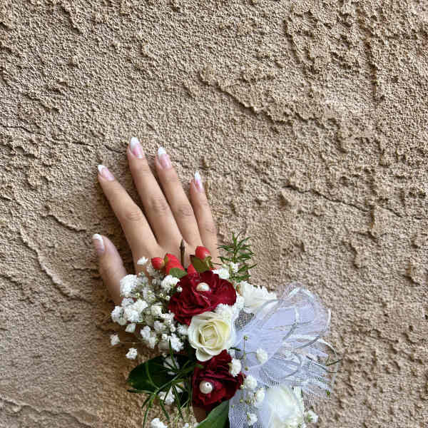 Hand wearing a floral wrist corsage with red and white roses
