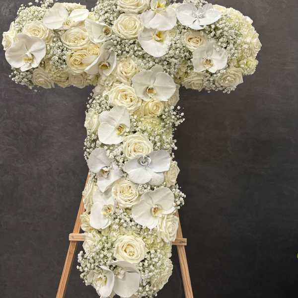 White floral cross on an easel with roses and orchids