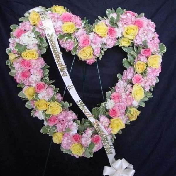 Heart-shaped floral wreath with pink and yellow roses and a white ribbon