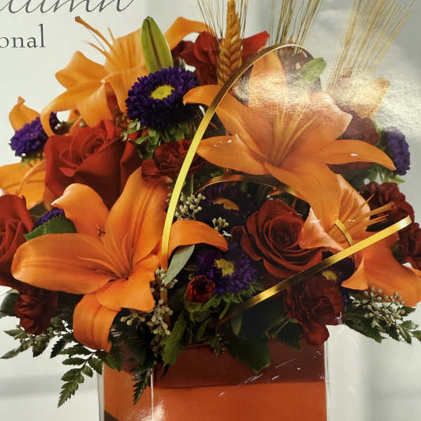 Orange lilies and red roses in a clear vase with gold ribbon