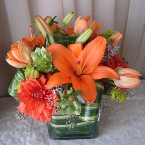 Orange lilies and dahlias arranged in a green glass vase