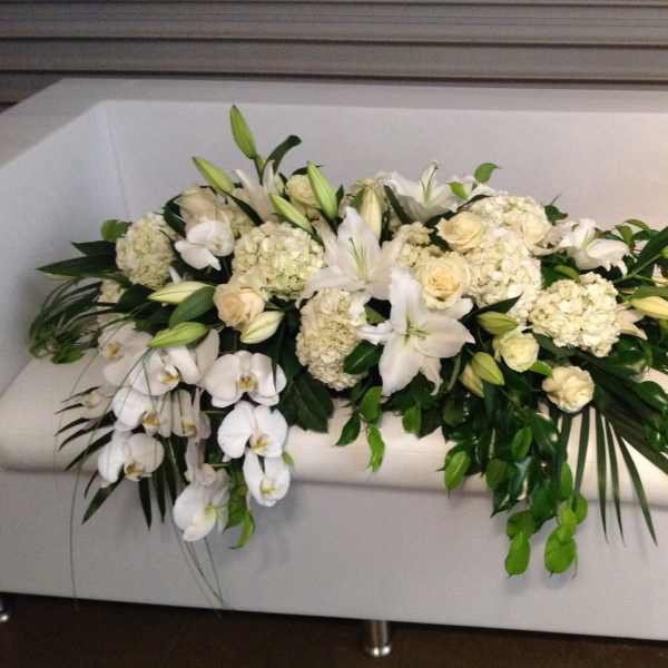 White floral arrangement with lilies, roses, and orchids on a white couch